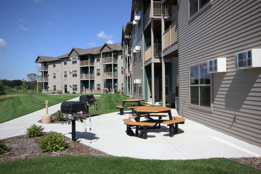 Apartment building with outdoor picnic tables and grill on a sunny day.