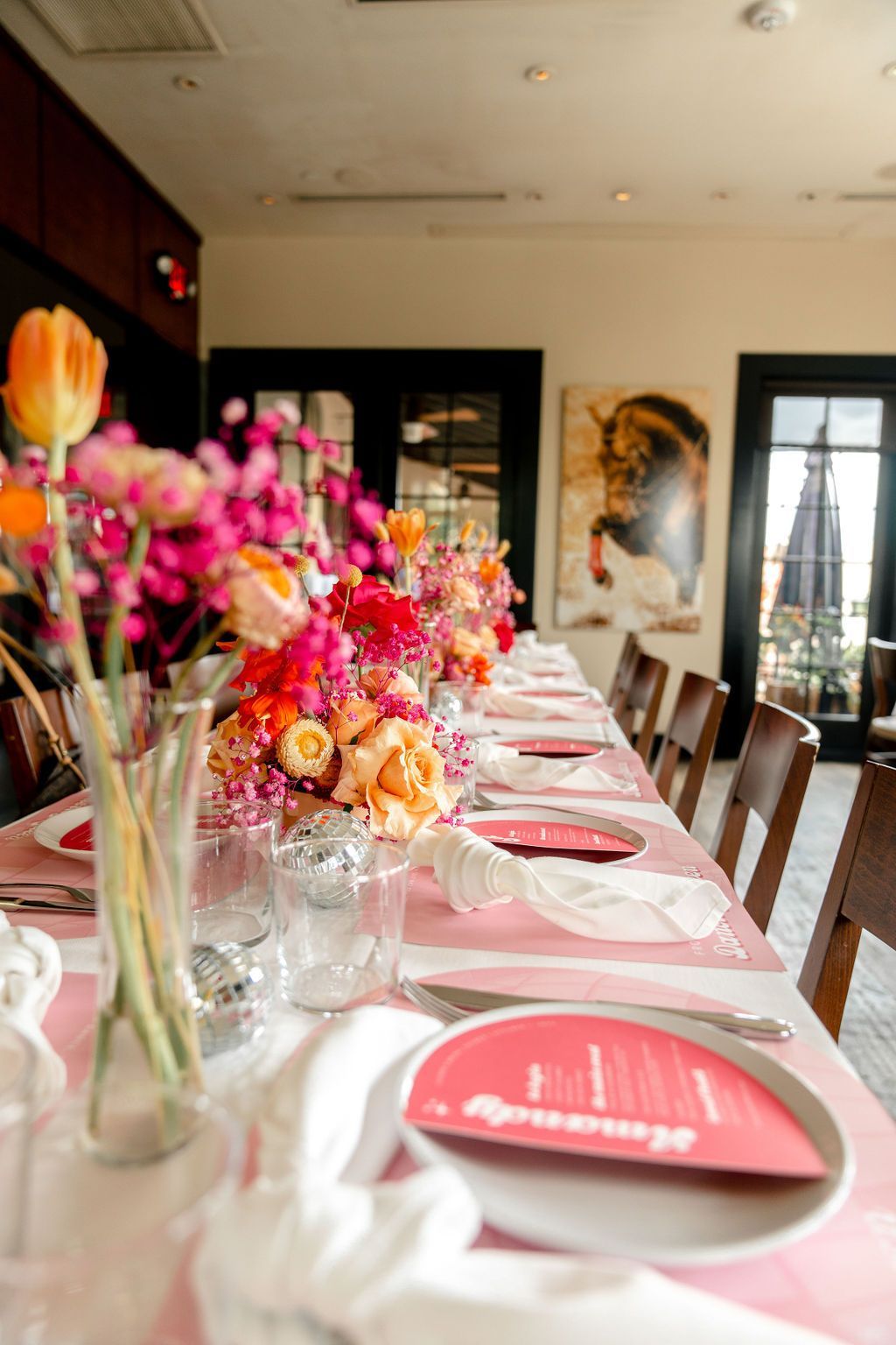 A long table with plates, utensils, and flowers on it. A long table with plates, utensils, and flowers on it.
