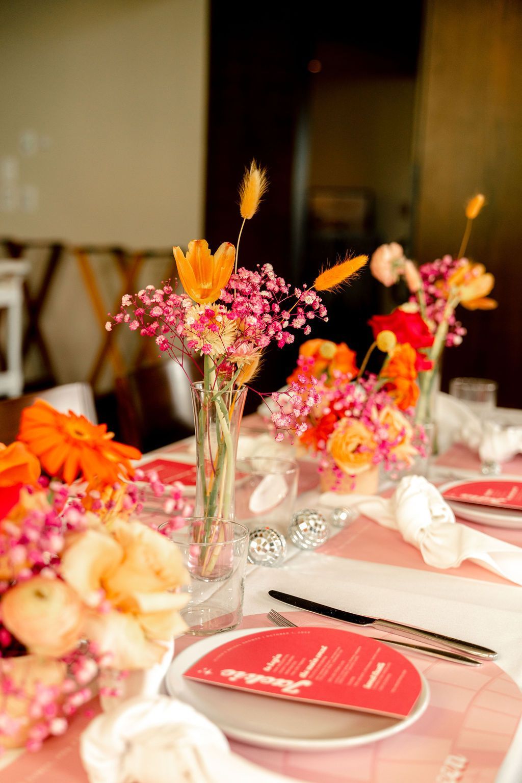 A table with plates, utensils, and colorful flowers on it. A table with plates, utensils, and colorful flowers on it.