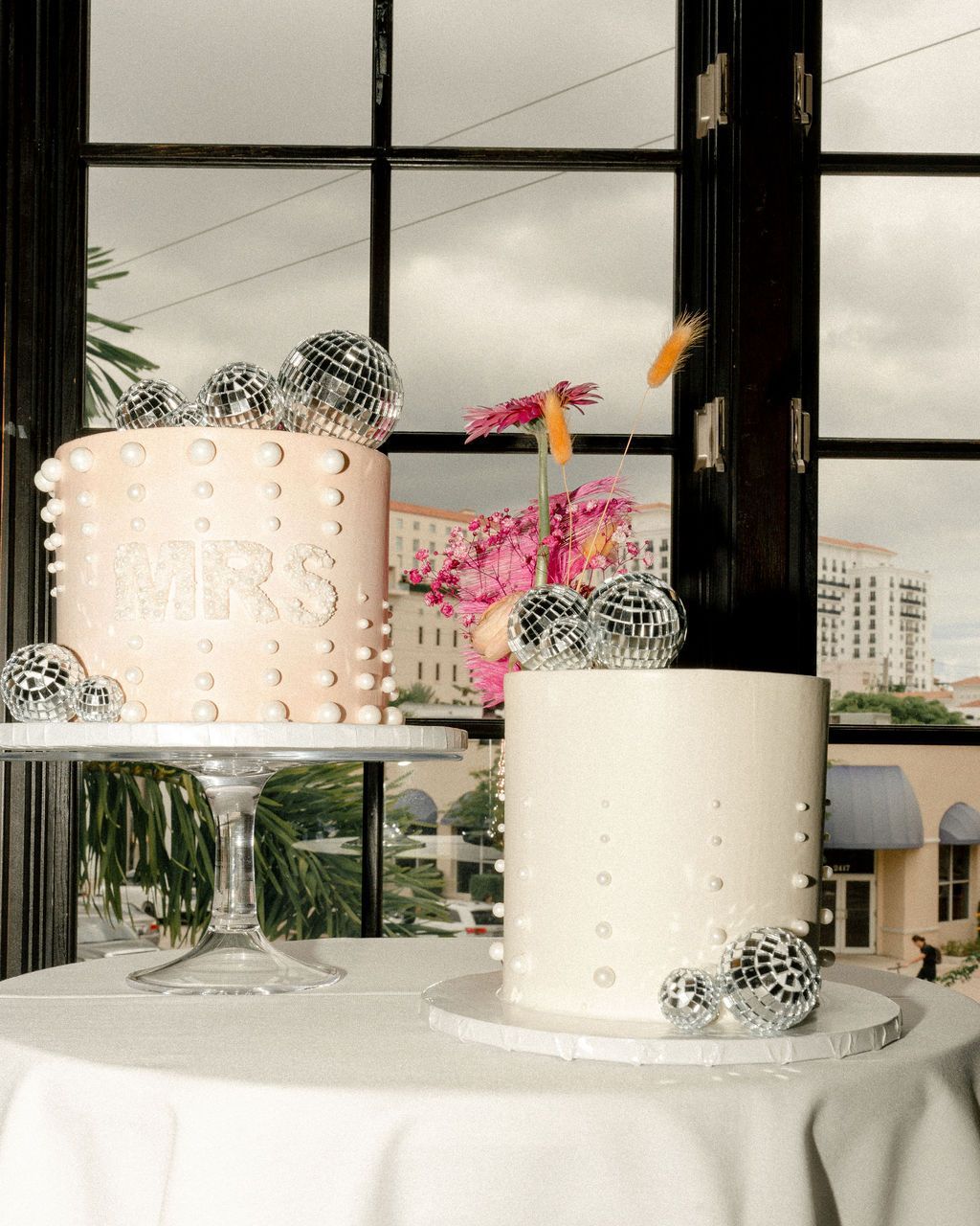 Two cakes are sitting on a table in front of a window Two cakes are sitting on a table in front of a window