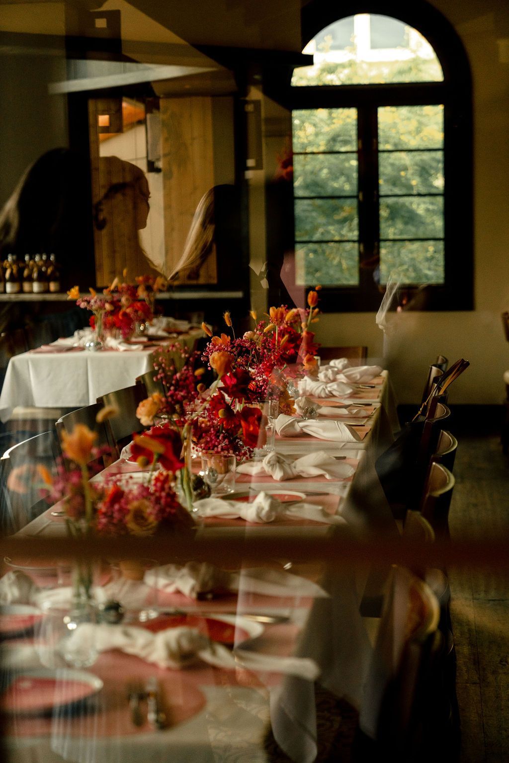 A long table in a restaurant with flowers on it A long table in a restaurant with flowers on it