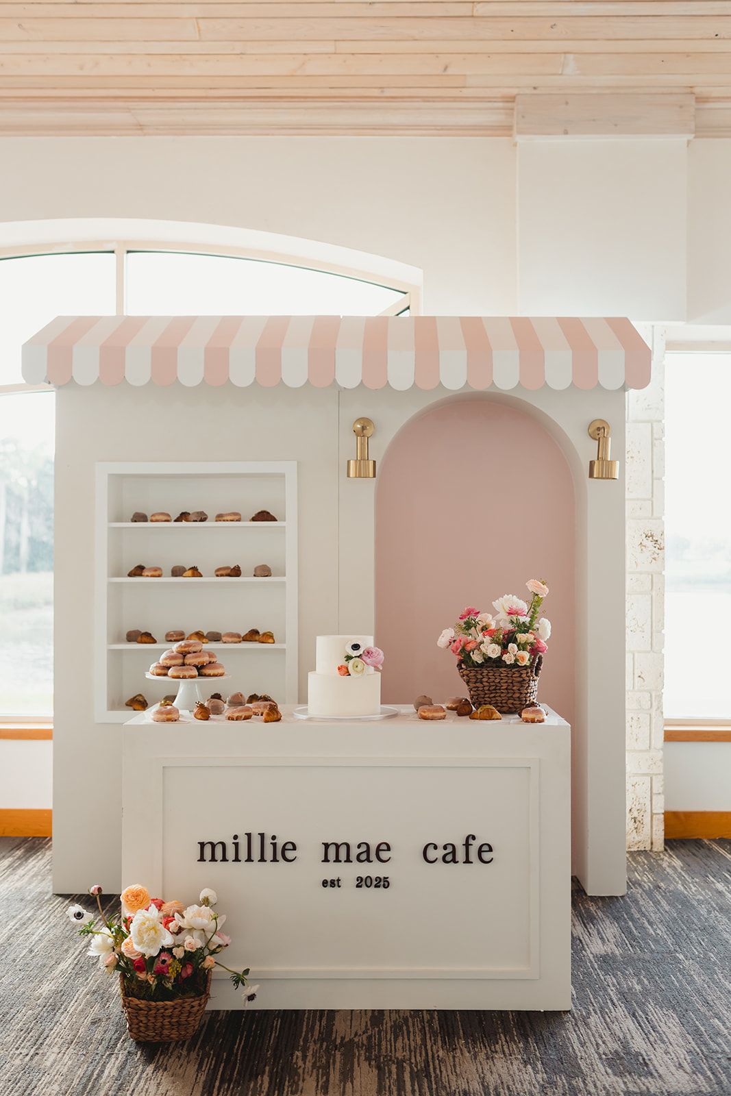 Bakery-inspired baby shower backdrop with blush pink arch, gold sconces, and scalloped awning 