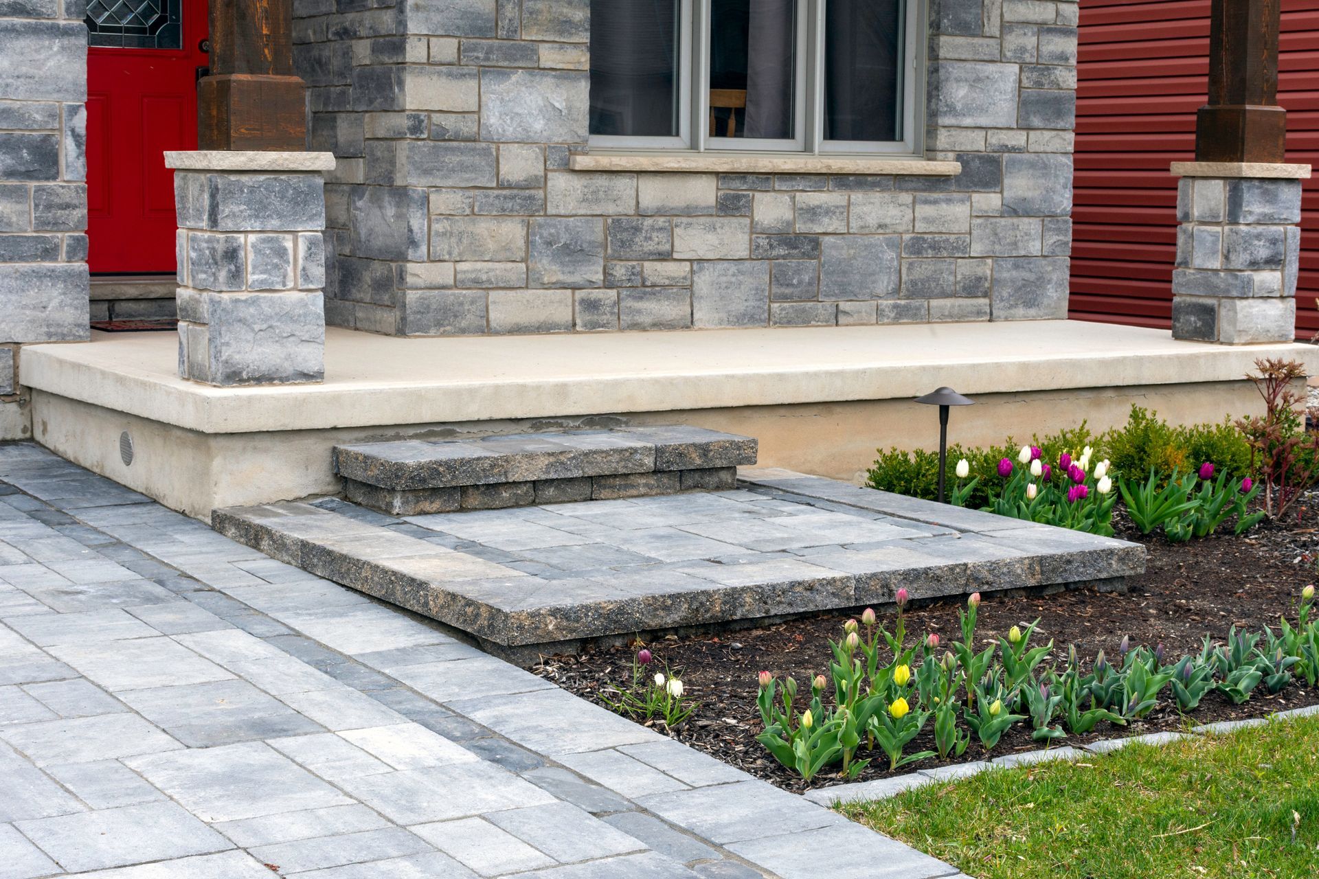Stone entrance with steps and pathway leading to a porch with brick facade and red door.