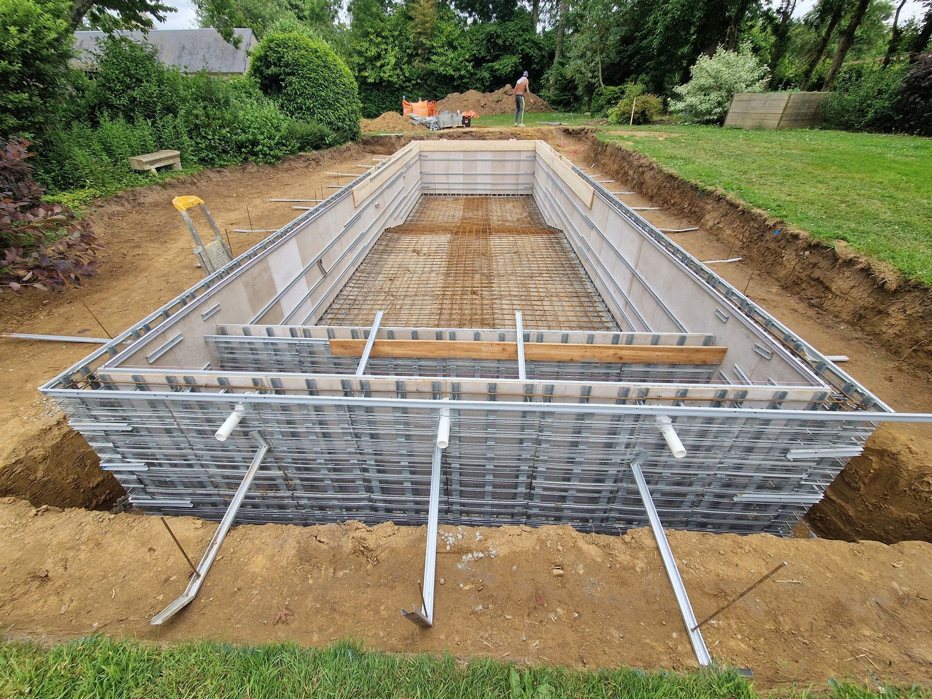 Construction of a rectangular in-ground pool, with concrete frame and rebar in a backyard.