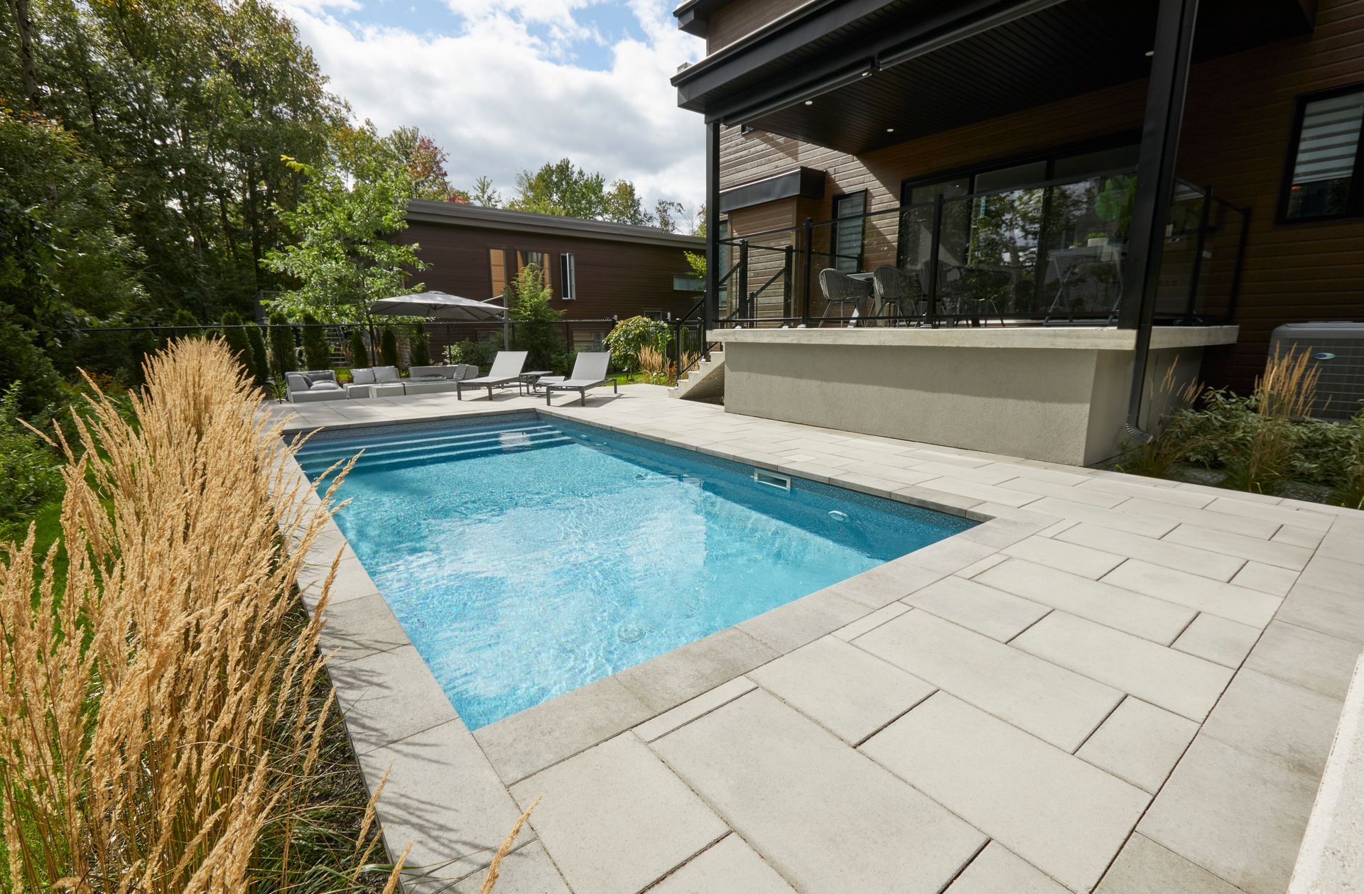 Poolside lounge area with sofas, umbrellas, and a view of trees and the sky.