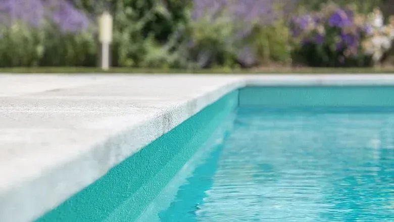Pool overlooking ocean with palm trees, lounge chairs, and green tropical water. Sunny day.