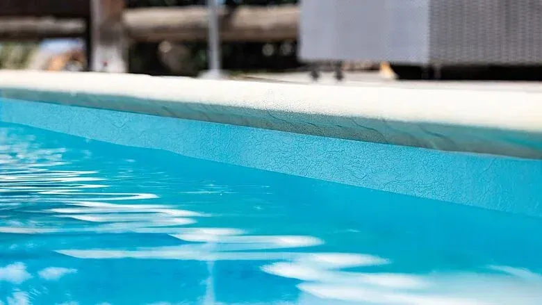 Pool overlooking ocean with palm trees, lounge chairs, and green tropical water. Sunny day.