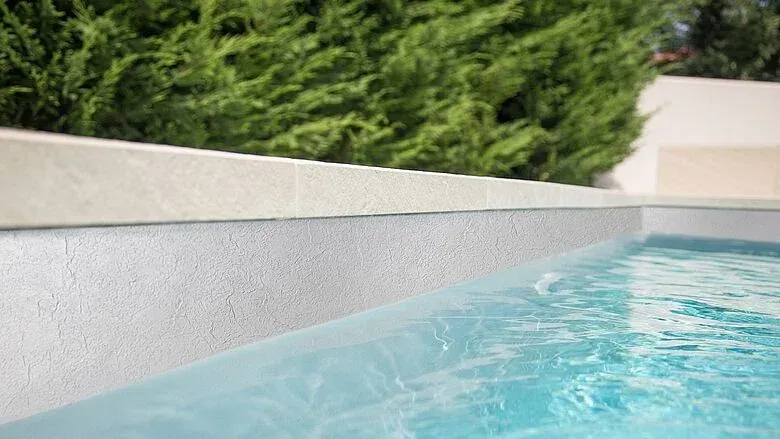 Pool overlooking ocean with palm trees, lounge chairs, and green tropical water. Sunny day.