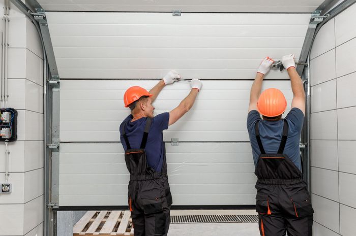 two men wearing hard hats are working on a garage door