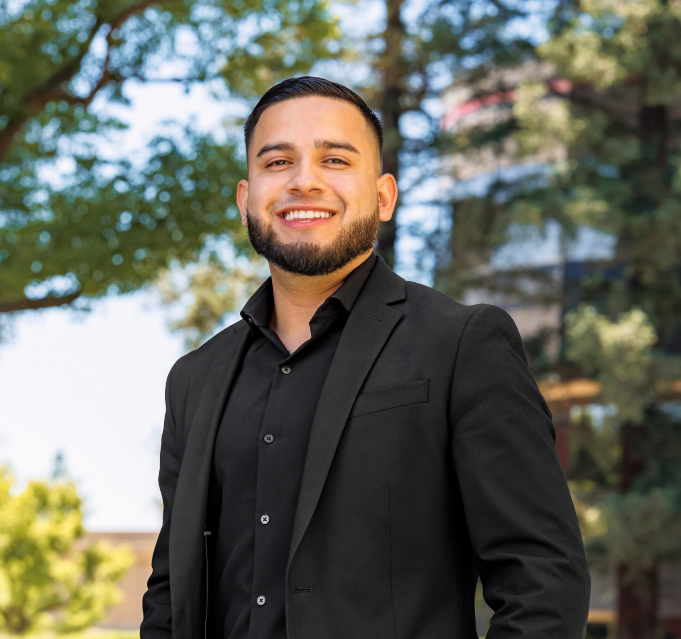 A man in a suit and black shirt is standing in the grass with his hands in his pockets.