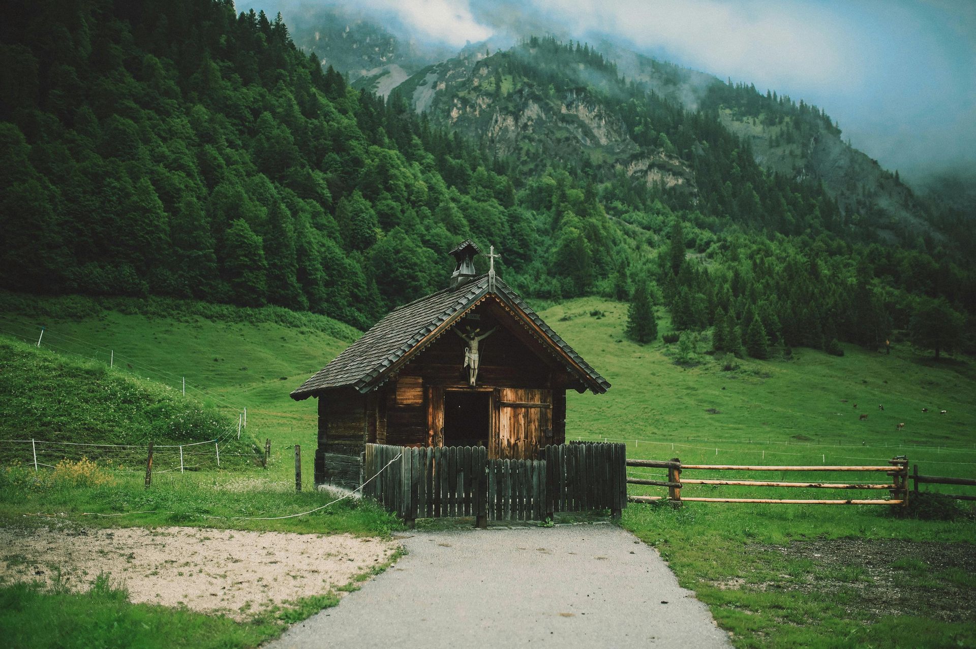 A small house in the middle of a grassy field with mountains in the background.