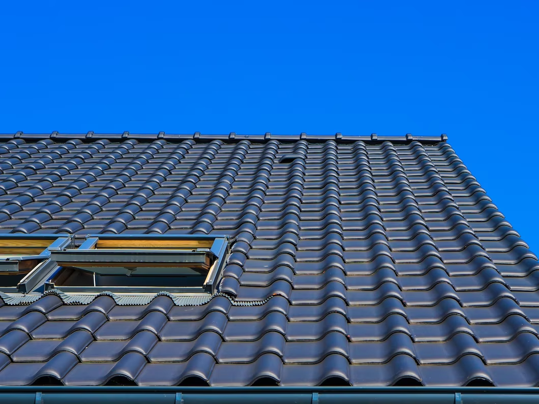 Dark blue tiled roof with open skylight against a bright blue sky.