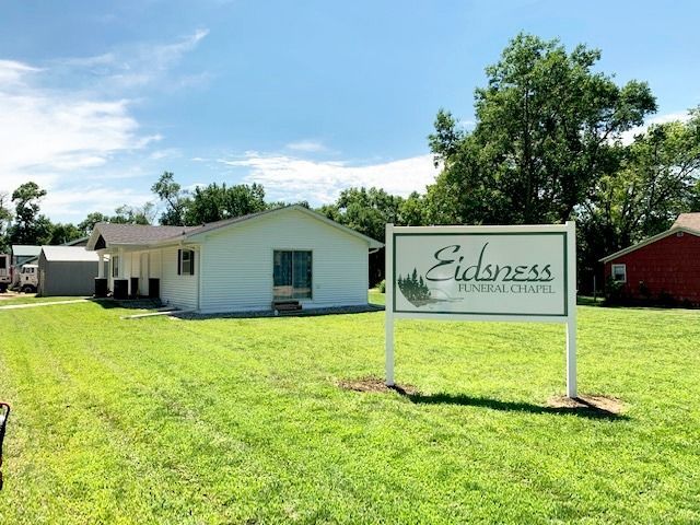 Spacious room with floral carpet, a sofa, chairs, and a small fridge. Neutral walls and overhead lighting.