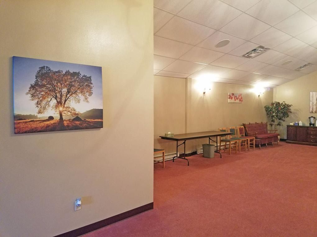 Spacious room with floral carpet, a sofa, chairs, and a small fridge. Neutral walls and overhead lighting.