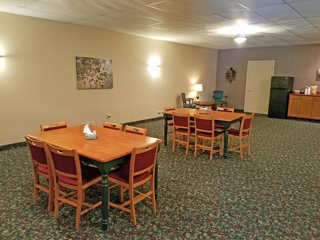 A room with tables and chairs, beige walls, patterned carpet, and a fridge.