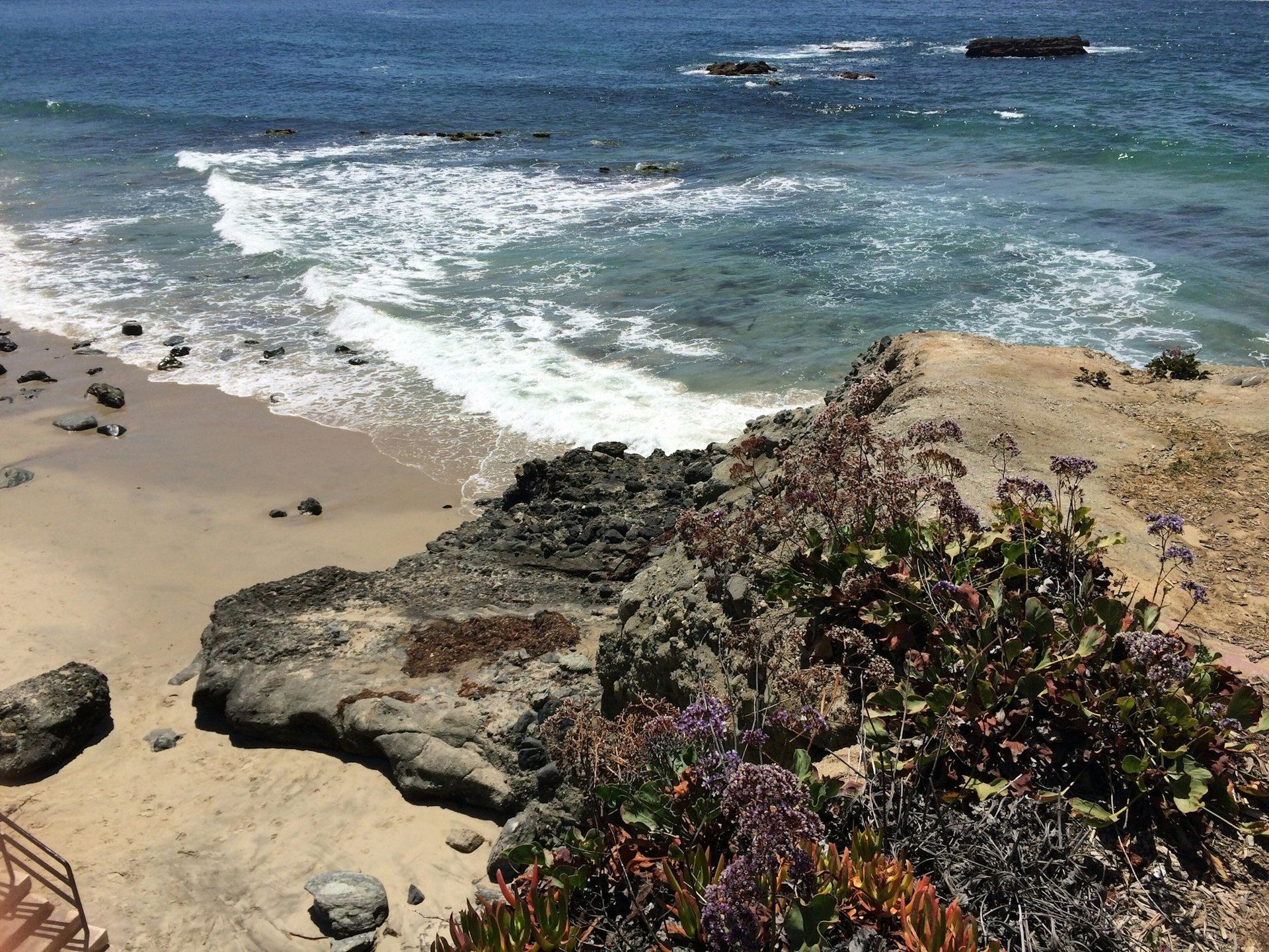 A view of a beach from a cliff overlooking the ocean.