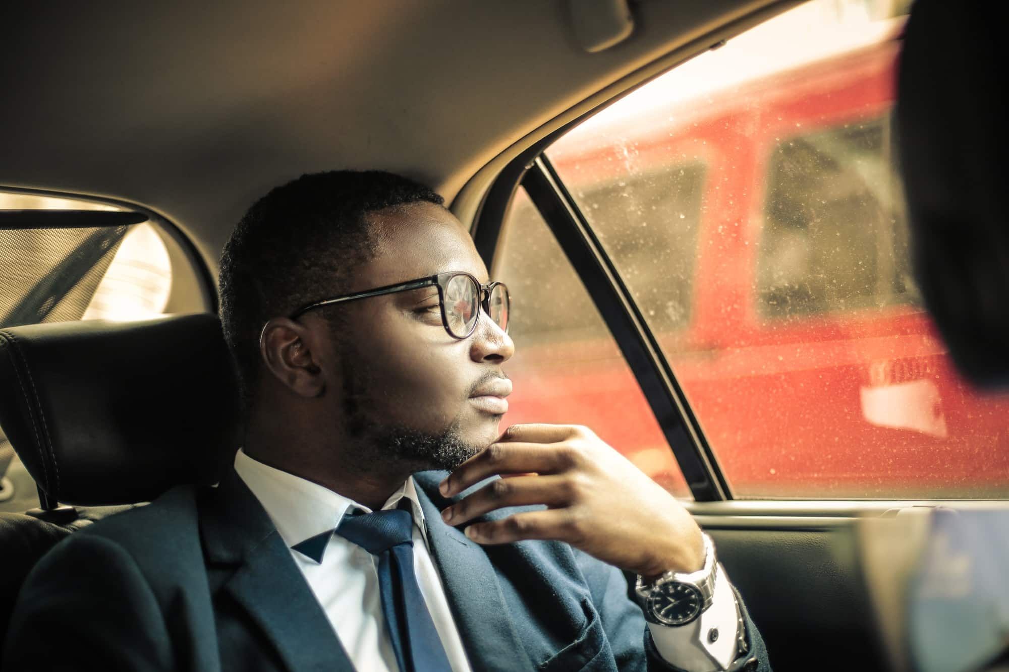 A man in a suit and tie is sitting in the back seat of a car looking out the window.