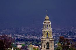 A large clock tower with a cross on top of it is in the middle of a city.