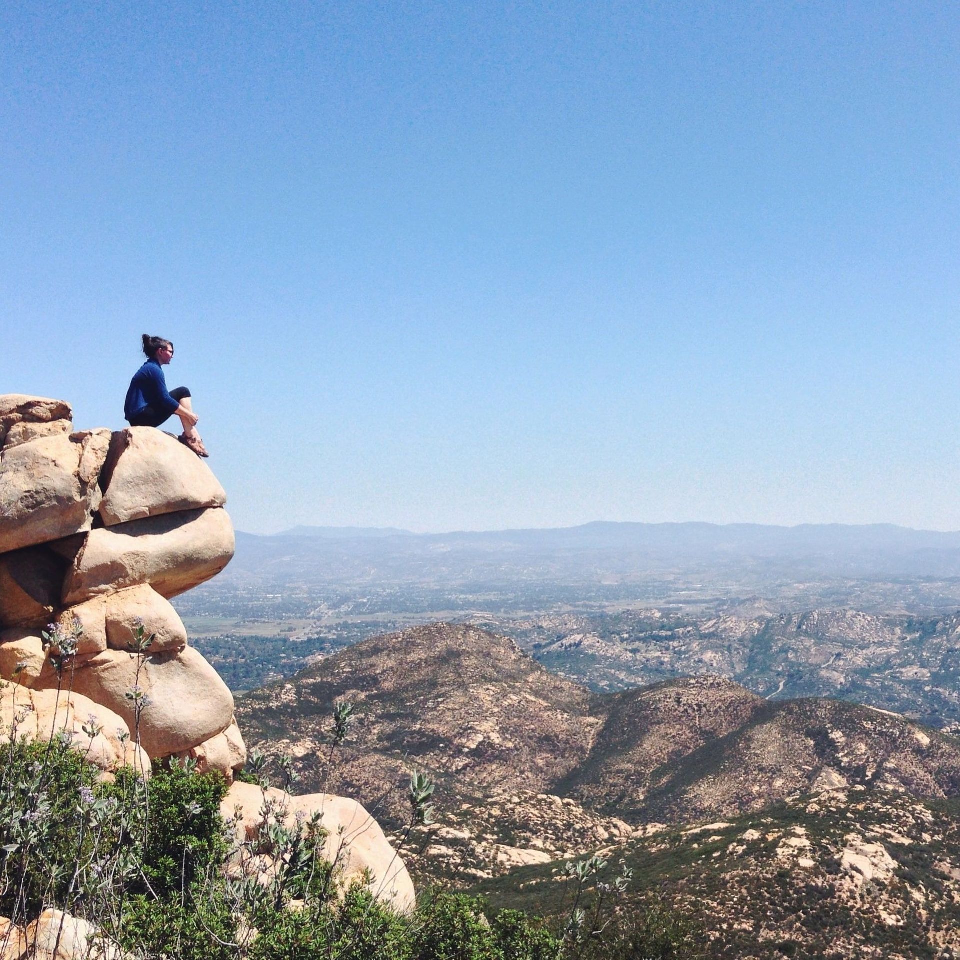 A person sitting on top of a rock overlooking a valley