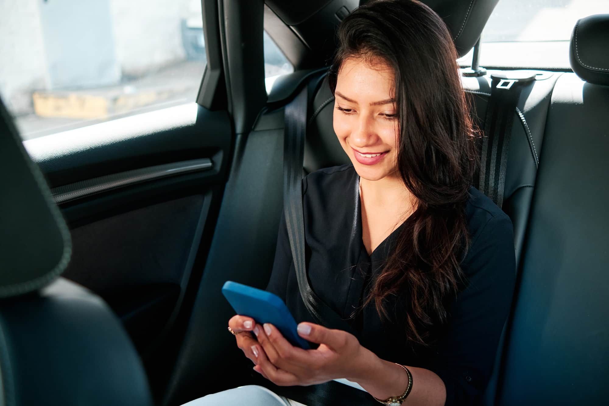 A woman is sitting in the back seat of a car looking at her cell phone.