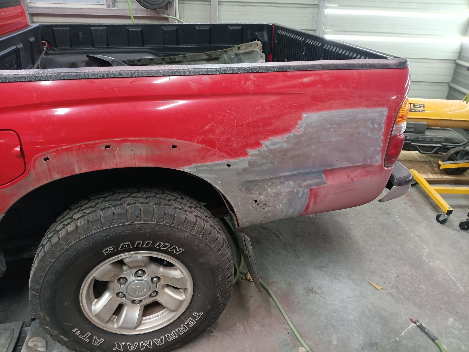A close-up of a bare metal car door showing rough, sanded spots, welding marks, and multiple small holes in the paneling.