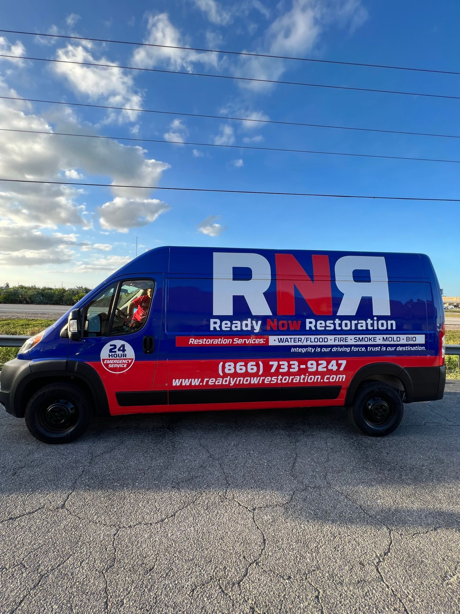 A blue and red van is parked in a gravel lot.