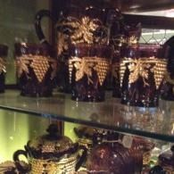 Decorative glass pitchers and mugs with gold-accented black designs on a shelf