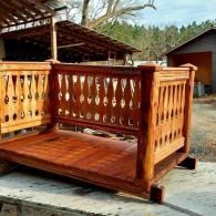 Wooden porch swing with ornate cutout sides on a driveway outdoors