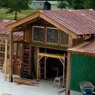Small unfinished wooden shed with open doorway, red metal roof, green siding, and a ladder inside