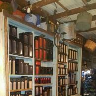 Shelves of bottled beverages and goods inside a rustic shop with a corrugated metal roof.
