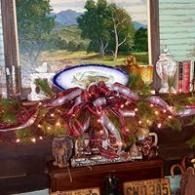 Decorated mantel with red bows, garland lights, dishes, and framed landscape art against a window