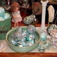 Bowl of silver and mint ornaments on a table with a white candlestick and floral decorations