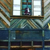 Leaning up guitar perched in a window above a weathered wooden wall with chevron siding