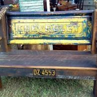 Weathered yellow and brown wooden truck tailgate with black license plate, parked on grass.