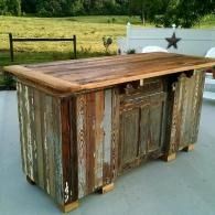 Rustic wooden kitchen island with distressed gray sides and a dark wood top outdoors on a driveway.