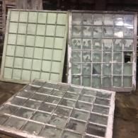 Old window panes and frames stacked against a wall, including a green pane and a clear glass section.