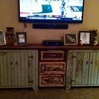 TV above a vintage wooden cabinet with framed photos and decorative items on either side
