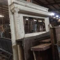 Old white wooden cabinet or mirror frame in a dim warehouse, with stacked furniture in front.