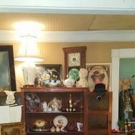 Cozy room with a lit lamp, wooden shelf of figurines, wall art, and a doorway to the right.