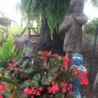 Garden statue amid red flowers and greenery, with a small blue bird sculpture nearby