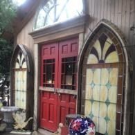 Red double doors on a rustic wooden building, flanked by stained-glass windows.