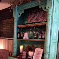 Turquoise display shelf with glass bottles, flowers, and framed decor in a rustic bar or café interior