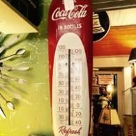 Coca-Cola bottle-shaped thermometer display in a store, with red, white, and green signage.