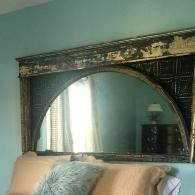 Antique dark wood arched mirror above a bed in a teal bedroom