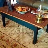 Wooden coffee table with brass lamp, bowl of fruit, and books on a patterned rug.