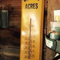 Vintage yellow-accented wall thermometer labeled “acres” beside stacked cans in a rustic interior