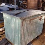 Weathered corrugated metal storage box with a slanted lid in a workshop or barn setting