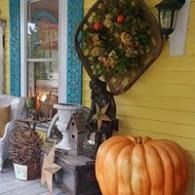 Pumpkin and fall porch decor beside a yellow house with wreaths and a lantern