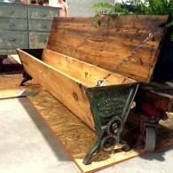 Antique wooden chest with open lid and metal hinges, sitting outdoors on a concrete patio.