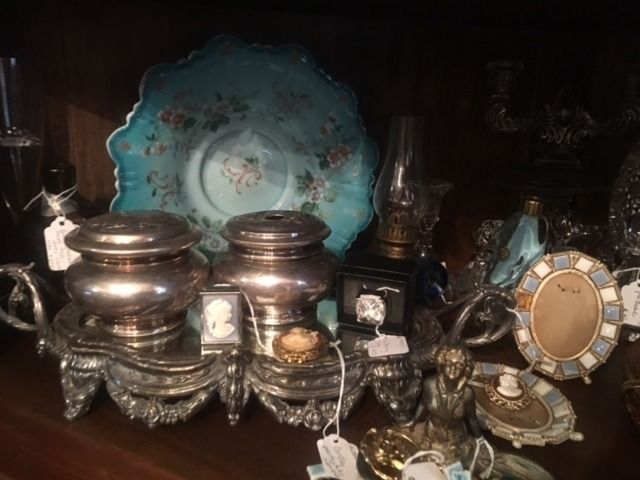 Antique silver tea set and blue decorative plate on a dark shelf, with a small oval vanity mirror.